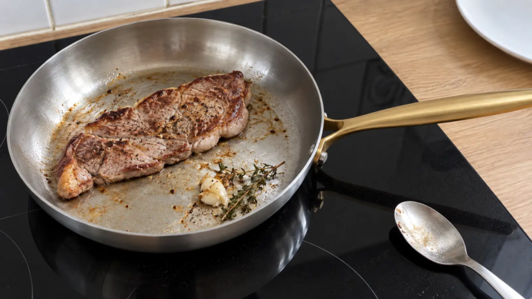 Poêle inox avec steak saisi, ail, thym, sur plaque induction