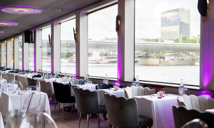 Tables d'un bateau-restaurant devant des baies vitrées donnant sur la Seine